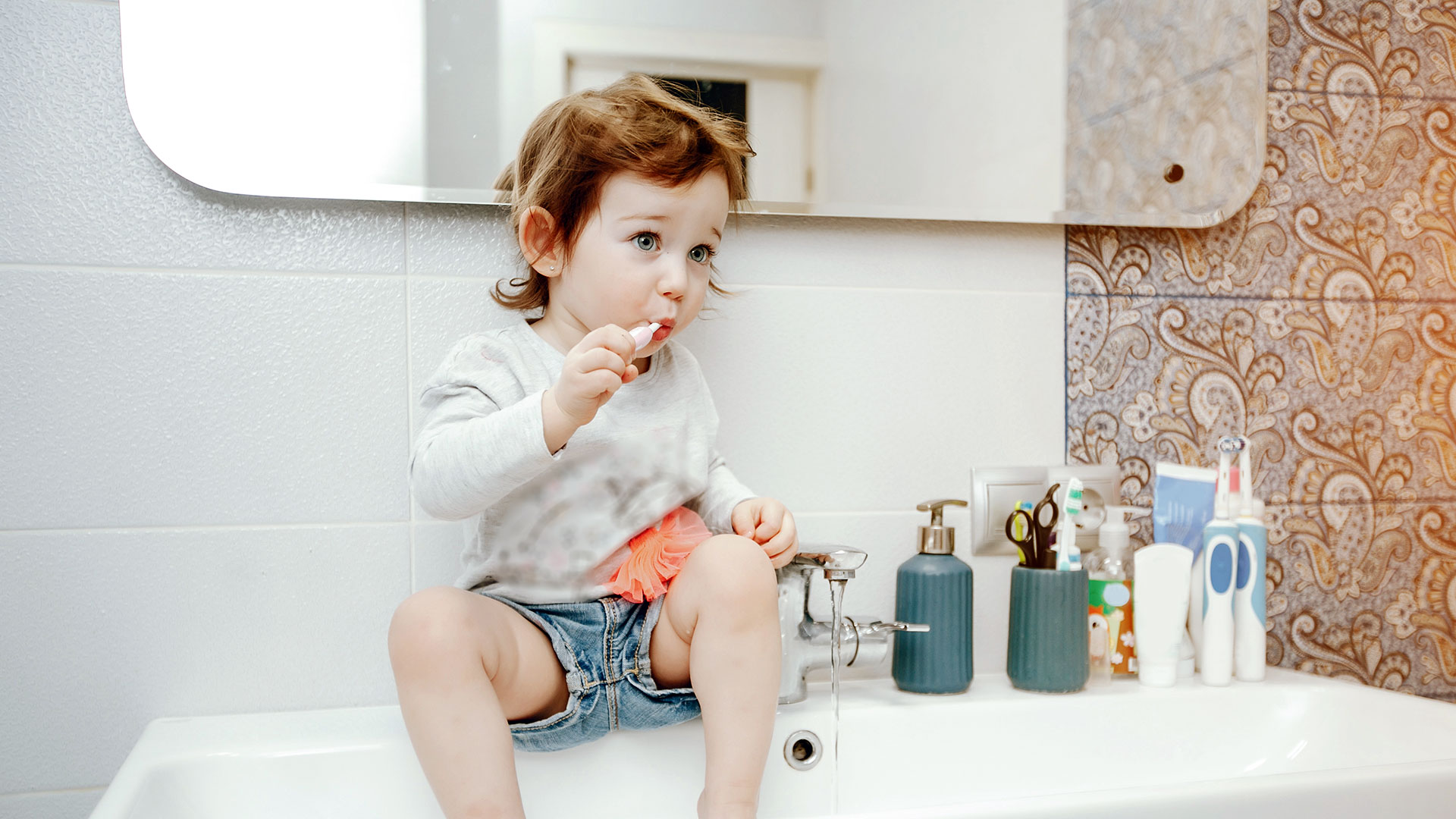 Bambina che si lava i denti con lo spazzolino seduta nel lavabo: igiene orale nei bambini e prevenzione dentale.