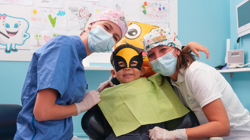 Immagine che mostra un bambino sorridente in compagia di due dentiste pediatriche