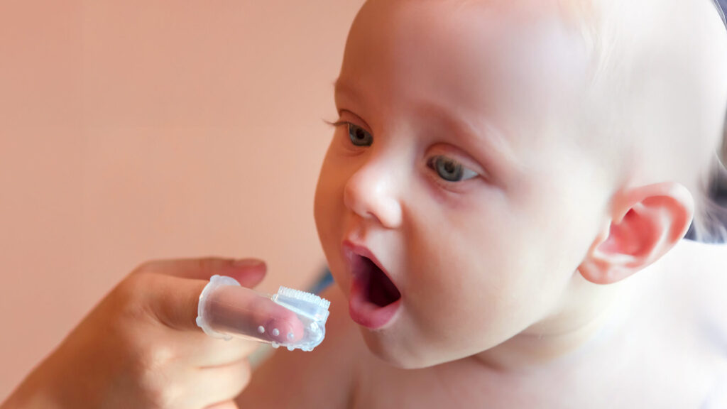 Foto di un bimbo di pochi mesi e di un genitore che si sta prendendo cura della sua igiene orale