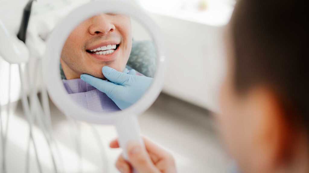 Foto di una persona che guarda il suo sorriso in uno specchio, dopo aver fatto estrazione e impianto dentale nella stessa seduta