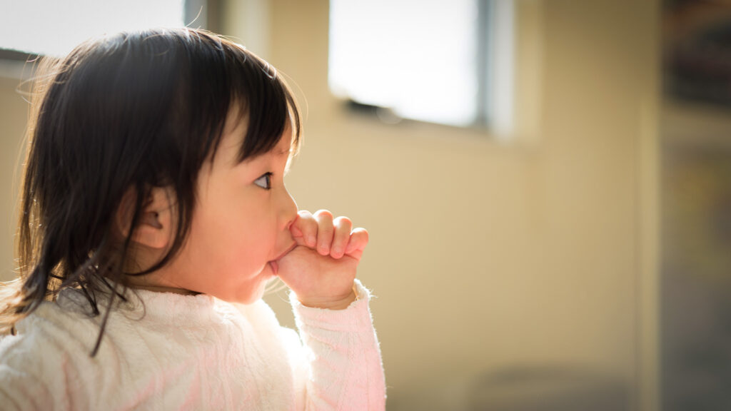 Foto di una bambina che si ciuccia il dito, una delle abitudini viziate che possono influenzare la crescita dei denti